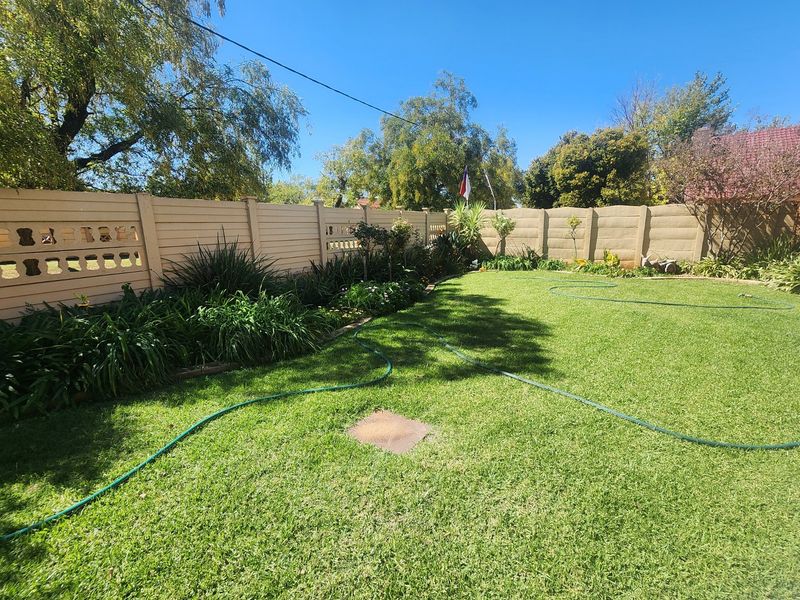 A well-maintained private garden featuring a lush green lawn and secure precast concrete boundary walling.