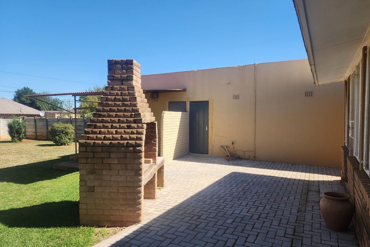 Rear exterior view featuring a paved patio area, a built-in brick braai, and a private garden space.