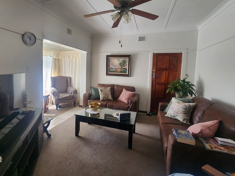 A living room featuring a ceiling fan, carpeted flooring, and a timber door, with visible signs of wear on the walls.