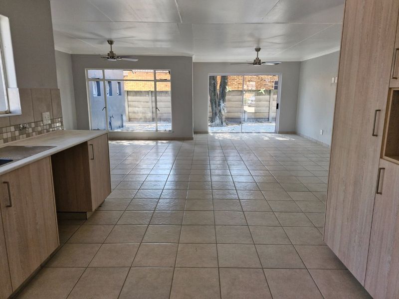 Spacious open-plan living area featuring tiled flooring, ceiling fans, and a functional kitchen layout with built-in cabinetry and direct access to the rear exterior.