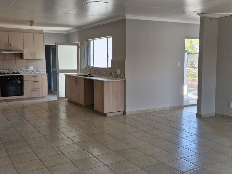 Spacious open-plan living area featuring a modern kitchen with built-in cabinetry, oven, hob, and tiled flooring throughout.