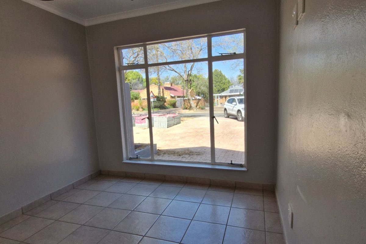 A bright, empty living room featuring neutral tiled flooring and a large window providing natural light and a view of the front exterior.