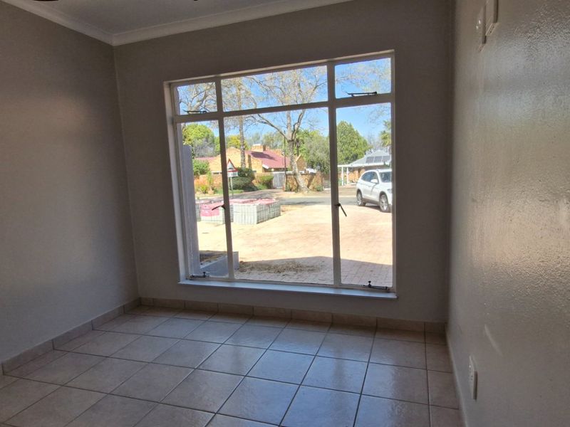 A bright, empty living room featuring neutral tiled flooring and a large window providing natural light and a view of the front exterior.