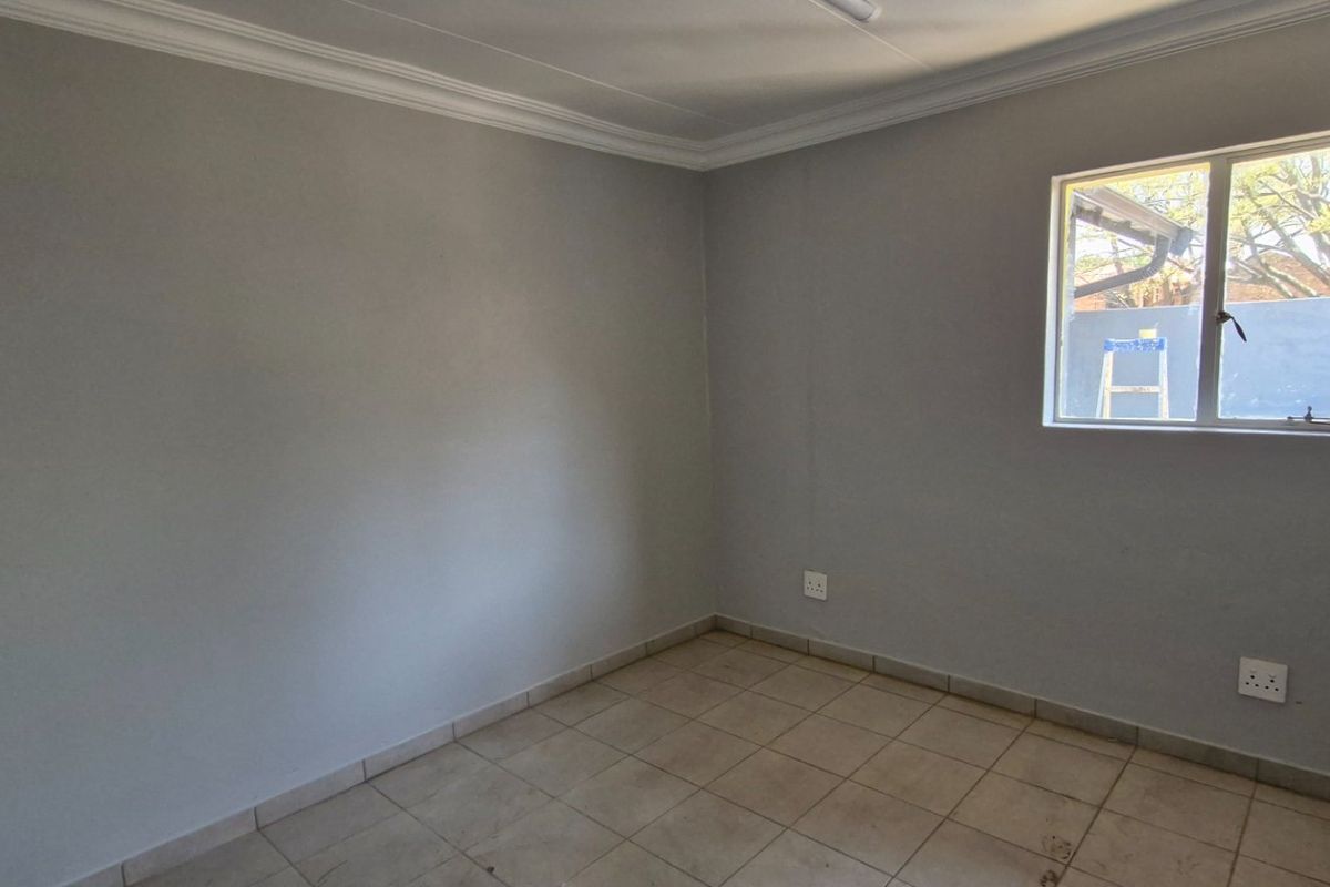 A clean, empty bedroom featuring neutral grey walls, tiled flooring, and a window providing natural light.