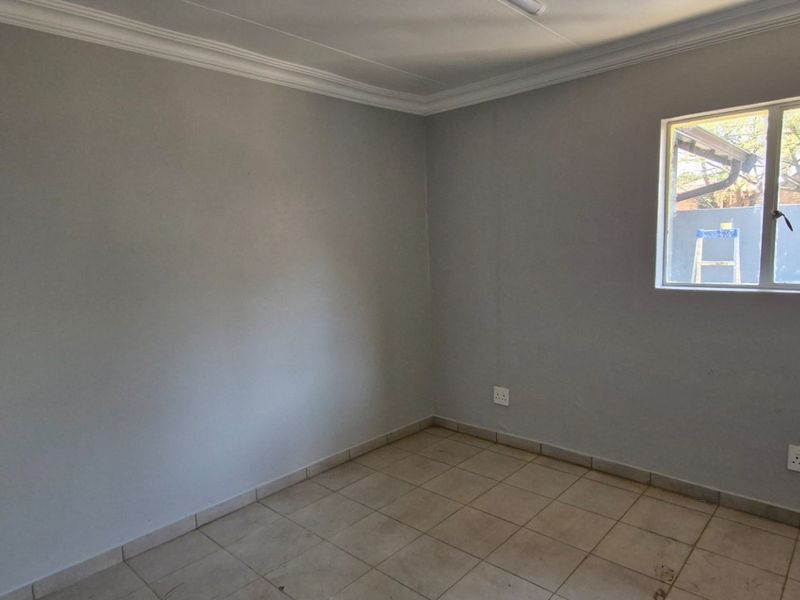 A clean, empty bedroom featuring neutral grey walls, tiled flooring, and a window providing natural light.