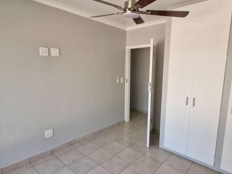A clean, empty bedroom featuring neutral tiled flooring, built-in white cupboards, and a ceiling fan, ready for personalization.