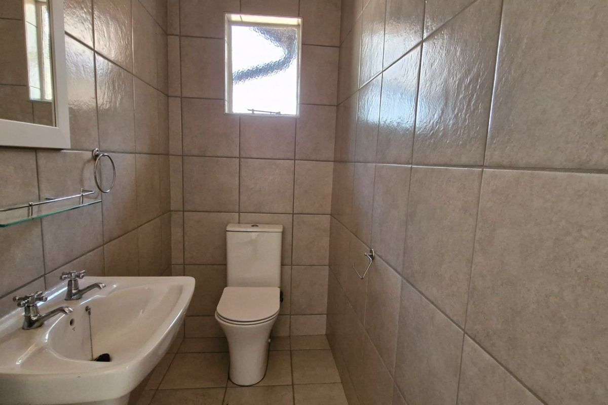 A compact, fully tiled bathroom featuring a pedestal basin, dual-handle faucet, and a standard toilet, finished with neutral wall and floor tiles.