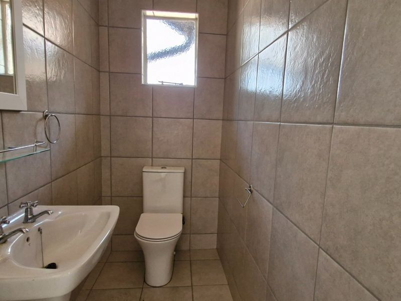 A compact, fully tiled bathroom featuring a pedestal basin, dual-handle faucet, and a standard toilet, finished with neutral wall and floor tiles.