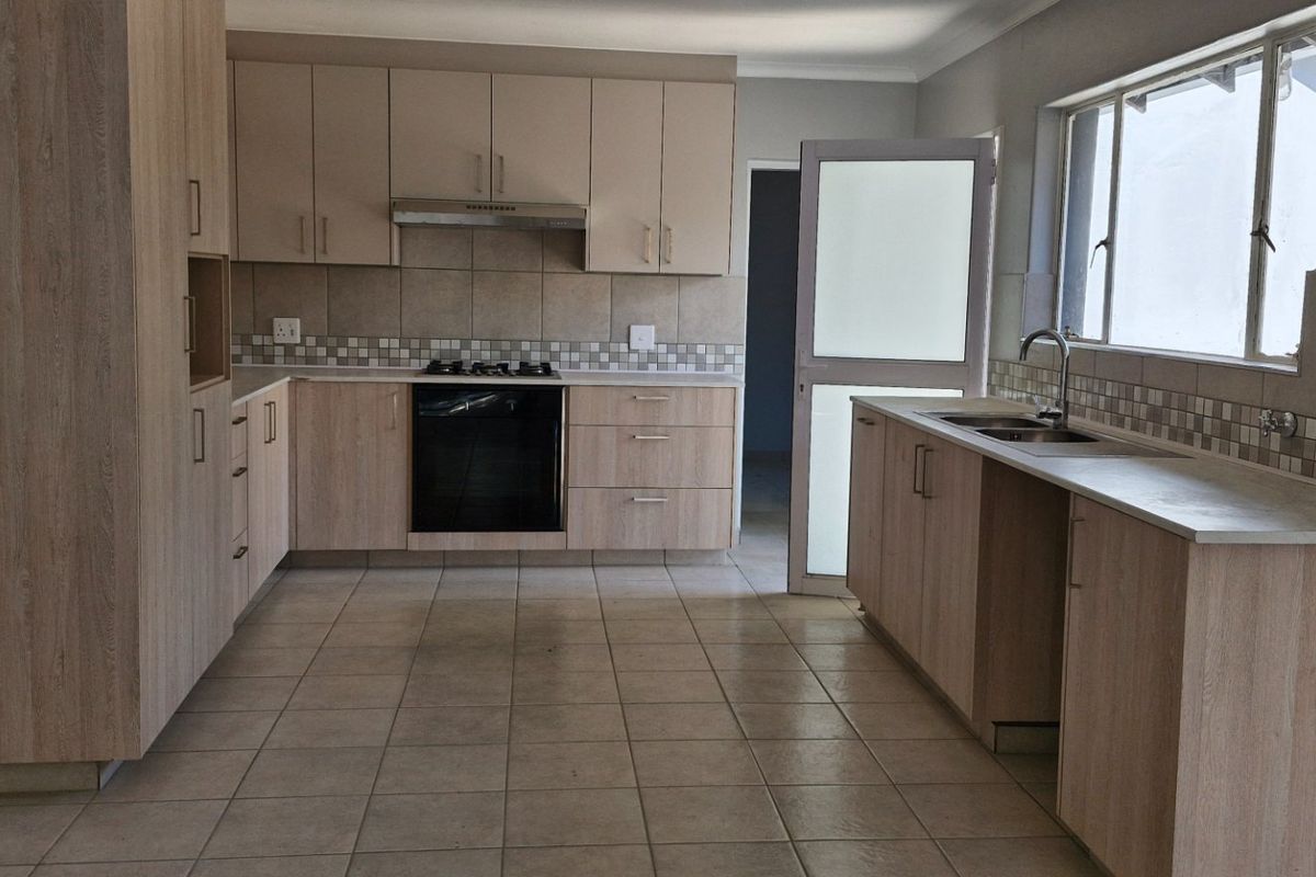 A spacious, empty kitchen featuring light wood-finish cabinetry, tiled flooring, a gas hob, built-in oven, and a functional layout with ample counter space.