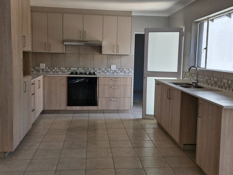 A spacious, empty kitchen featuring light wood-finish cabinetry, tiled flooring, a gas hob, built-in oven, and a functional layout with ample counter space.