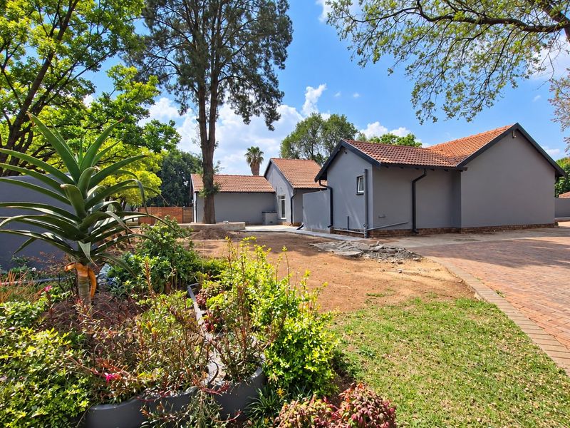Rear view of the property featuring a grey exterior finish, terracotta roof tiles, and a paved driveway with ongoing landscaping work.