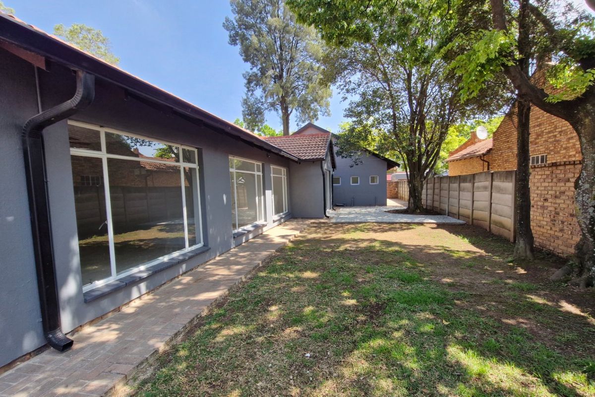 A rear exterior view of the property featuring a paved walkway, large windows, and a private garden area enclosed by boundary walls.