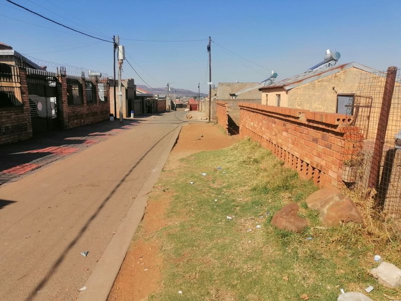 A street view showing the residential neighbourhood approach with brick boundary walls, solar water heaters, and paved access roads.