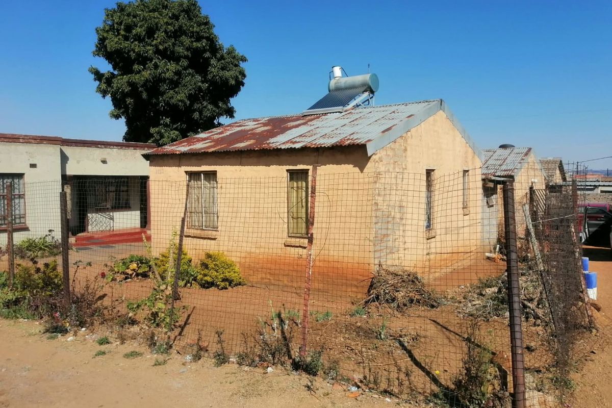 Front view of a detached house featuring a corrugated iron roof with a solar water heater and perimeter wire mesh fencing.