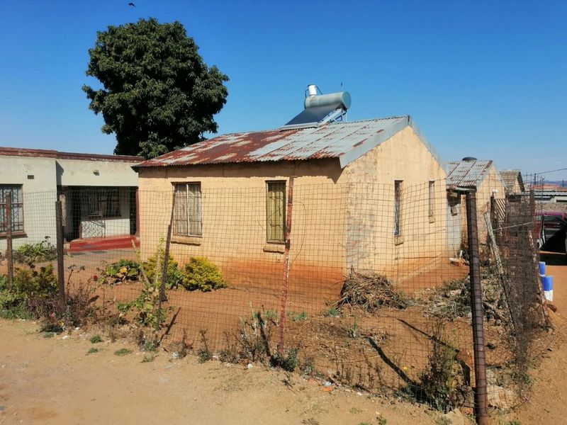 Front view of a detached house featuring a corrugated iron roof with a solar water heater and perimeter wire mesh fencing.