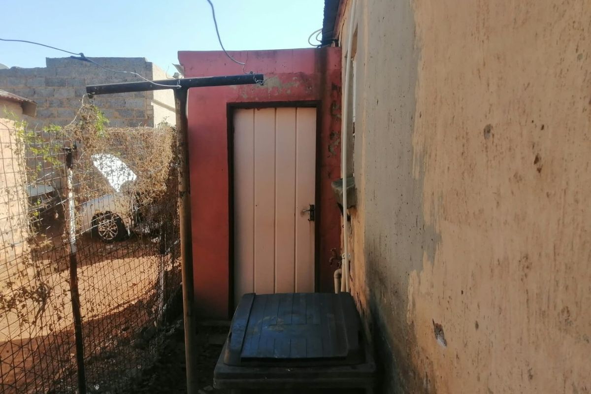 A view of the rear exterior area showing a side door, weathered wall finishes, and wire mesh fencing.