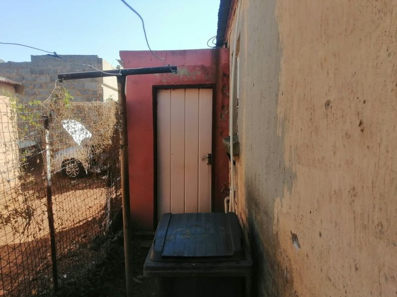 A view of the rear exterior area showing a side door, weathered wall finishes, and wire mesh fencing.