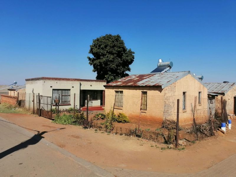 Front view of a residential property featuring a metal roof with a solar water heater, security bars, and perimeter wire fencing.