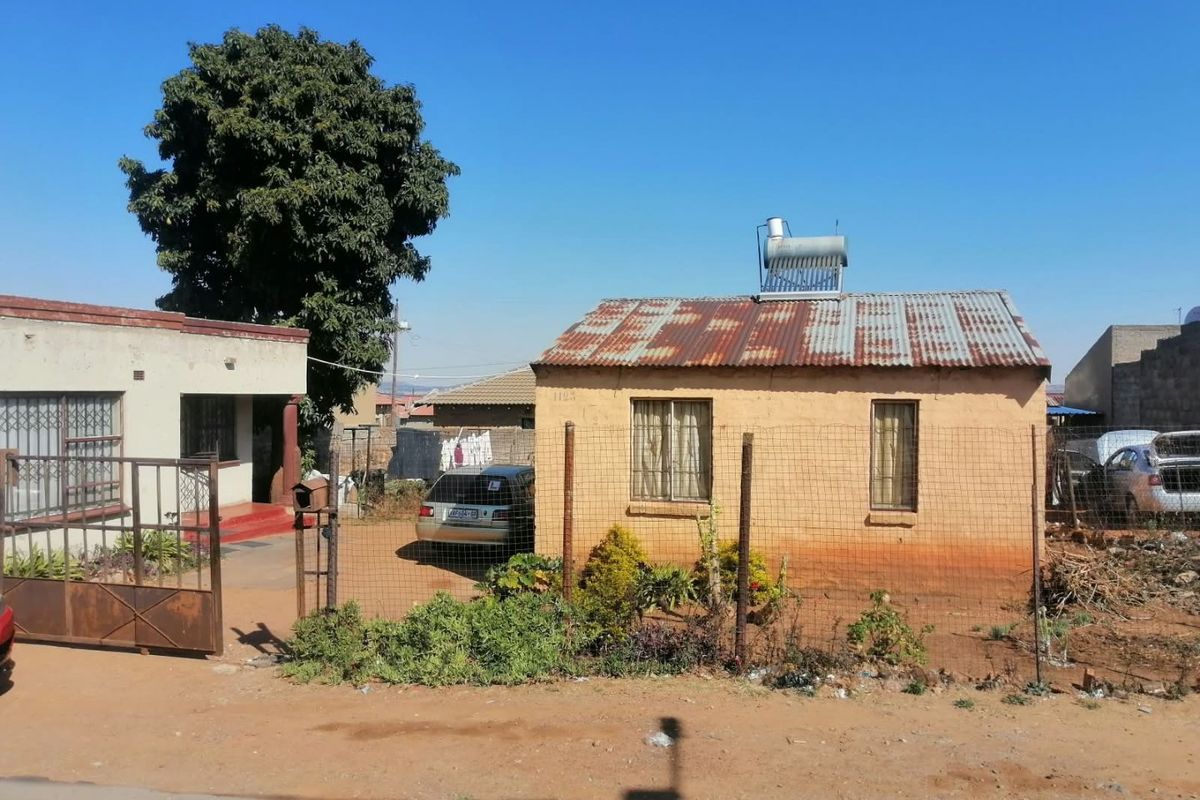 Front view of a single-story residential property featuring a corrugated iron roof with a solar water heater and perimeter wire fencing.