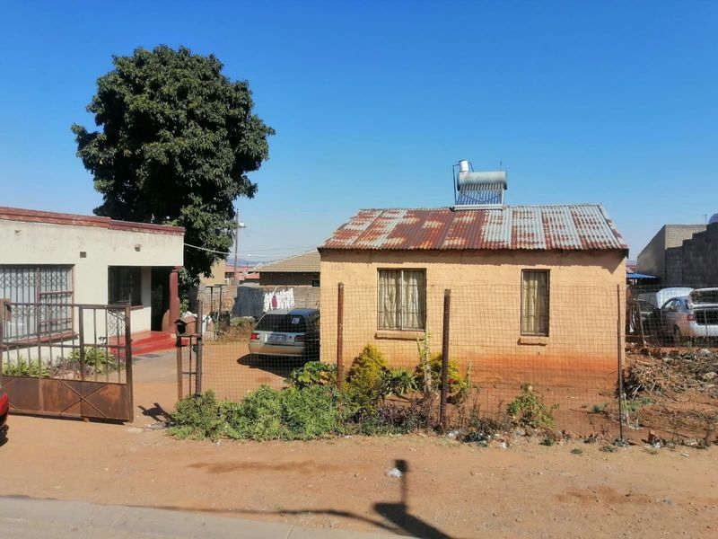 Front view of a single-story residential property featuring a corrugated iron roof with a solar water heater and perimeter wire fencing.