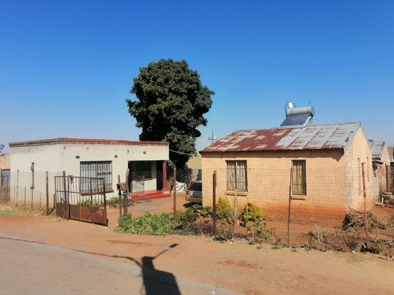Front view of a residential property featuring a corrugated iron roof with a solar geyser, security fencing, and gated entrance.