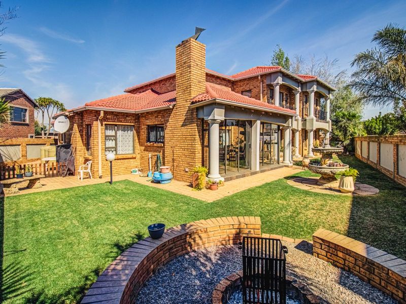 Rear view of a double-story brick house featuring a covered patio, stone columns, a built-in brick fire pit, and a landscaped garden.