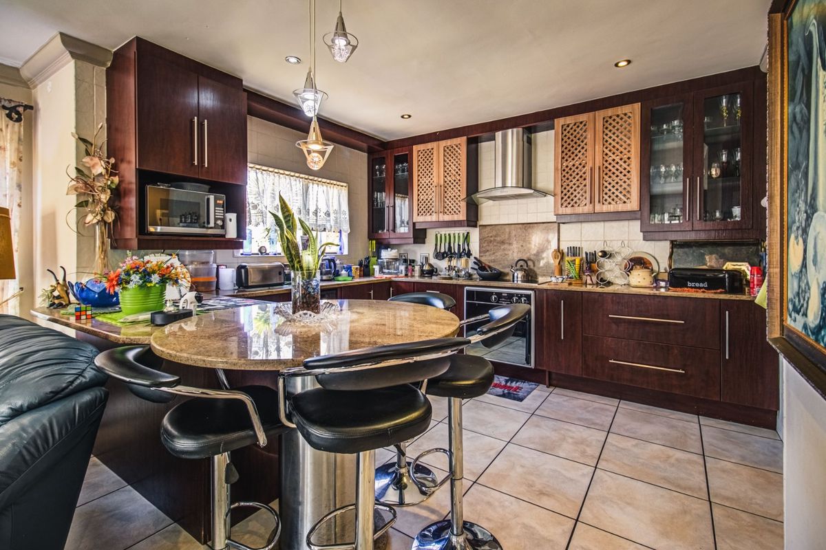 A functional kitchen featuring dark wood cabinetry, granite countertops, a built-in oven, stainless steel extractor fan, and tiled flooring with a breakfast nook.