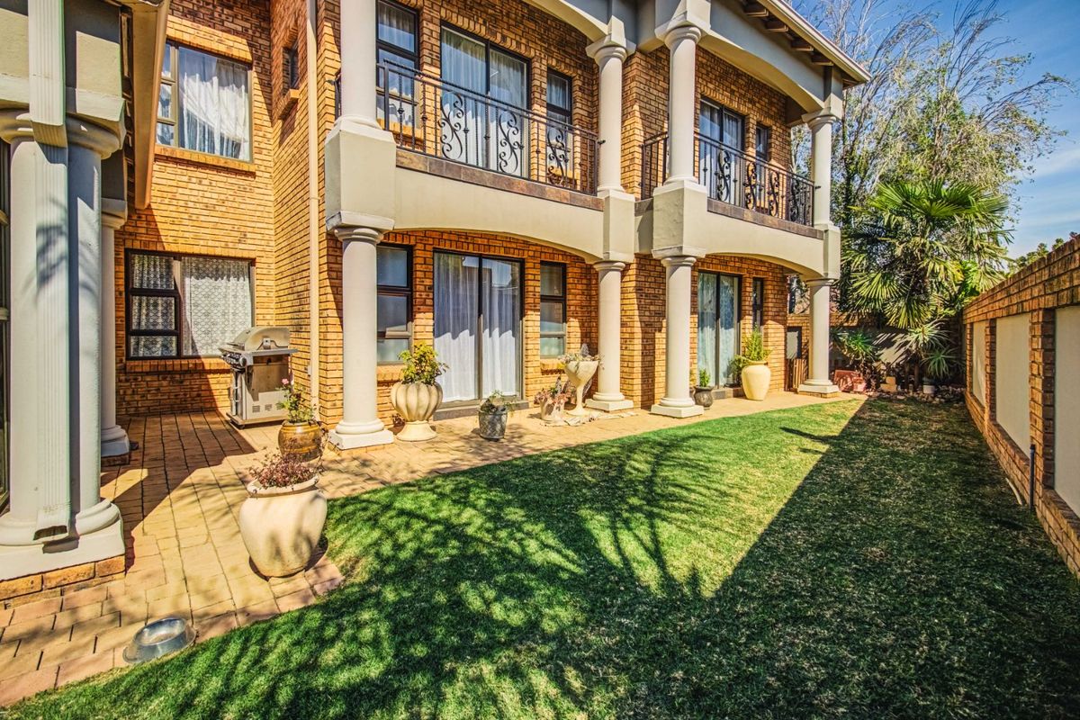 Rear view of a two-story brick house featuring a covered patio, upper-level balconies with wrought iron railings, and a well-maintained garden area.