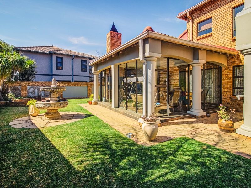 A well-maintained rear garden featuring a paved patio area, a stone fountain, and a covered outdoor living space with brick exterior finishes.