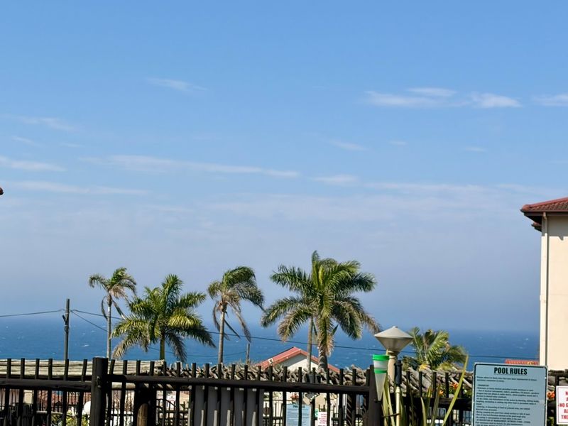 A scenic view of the ocean framed by apartment building structures, featuring palm trees and a clear blue sky.