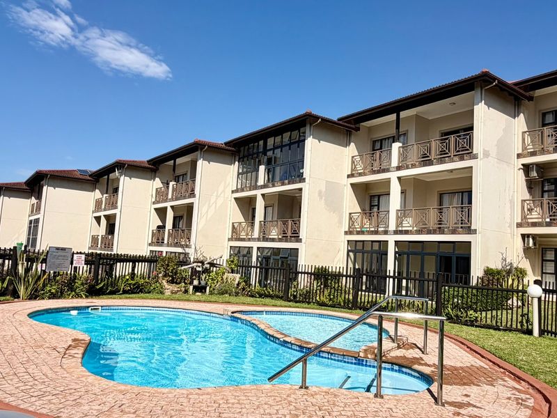 Communal swimming pool area featuring a paved surround and metal fencing, set against the exterior facade of a multi-story apartment complex.