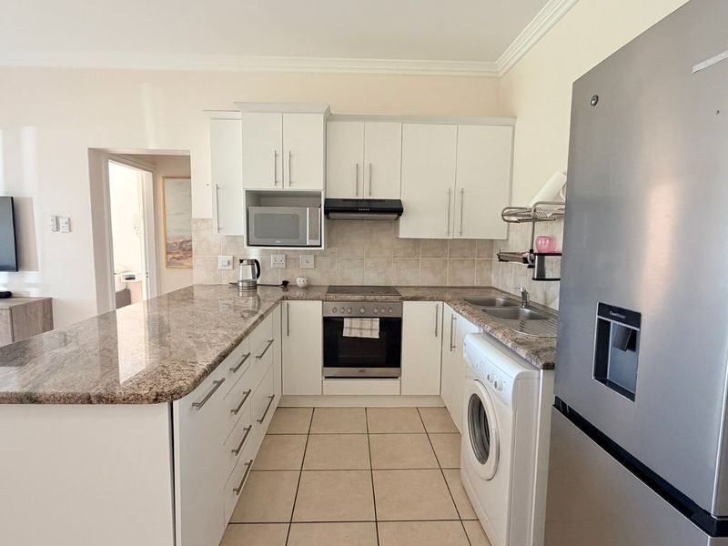 Open-plan kitchen featuring granite countertops, white cabinetry, built-in oven, hob, extractor fan, and integrated laundry appliance space.