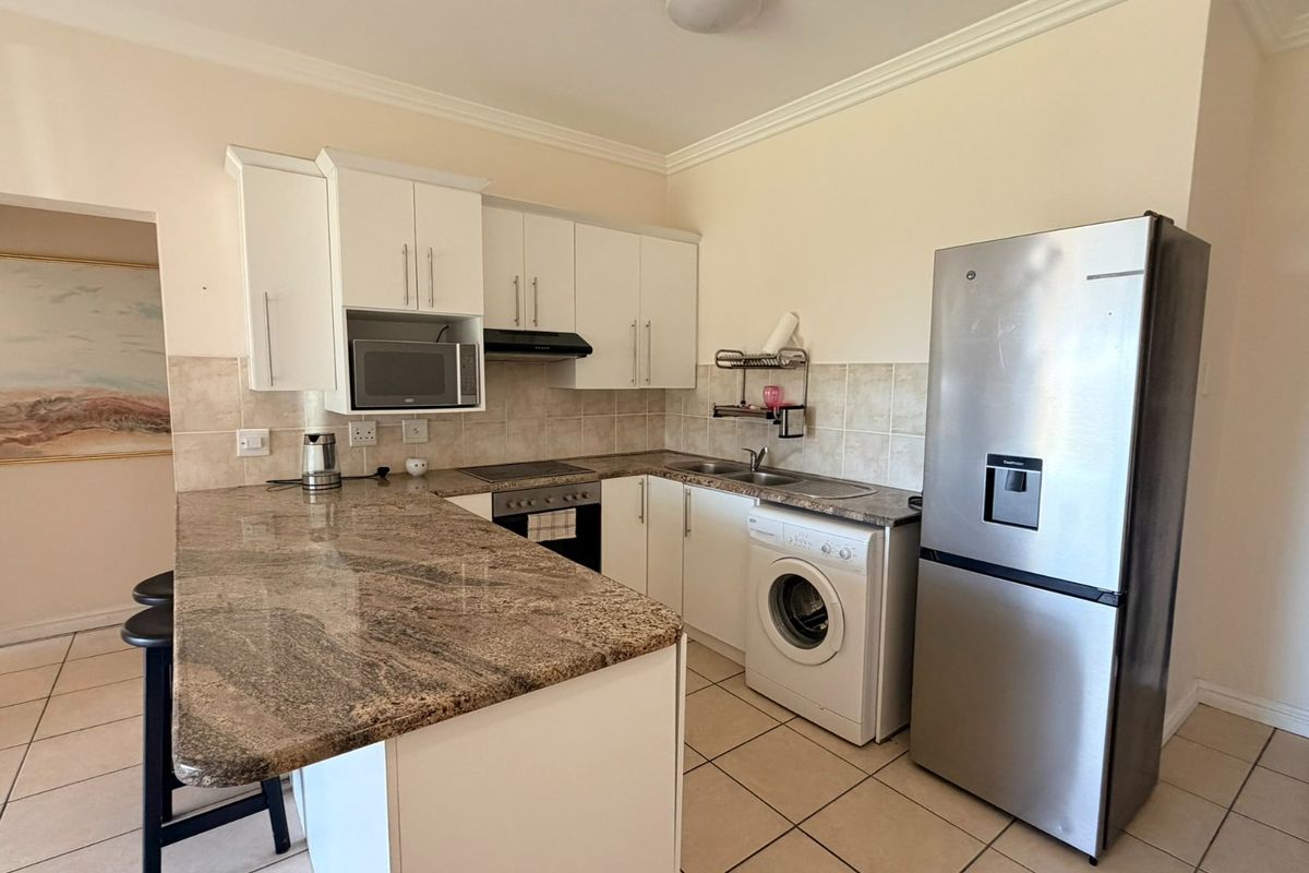 Functional kitchen featuring granite countertops, white cabinetry, built-in oven, hob, extractor fan, and integrated space for a washing machine.
