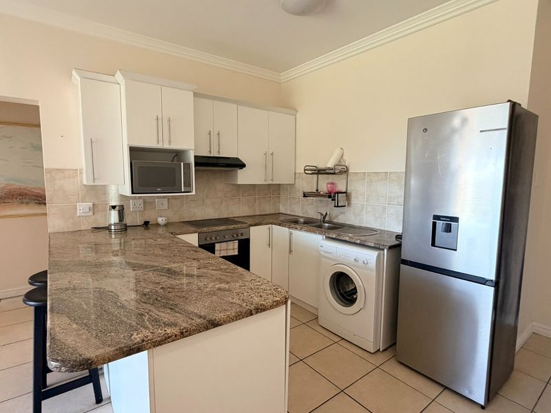 Functional kitchen featuring granite countertops, white cabinetry, built-in oven, hob, extractor fan, and integrated space for a washing machine.