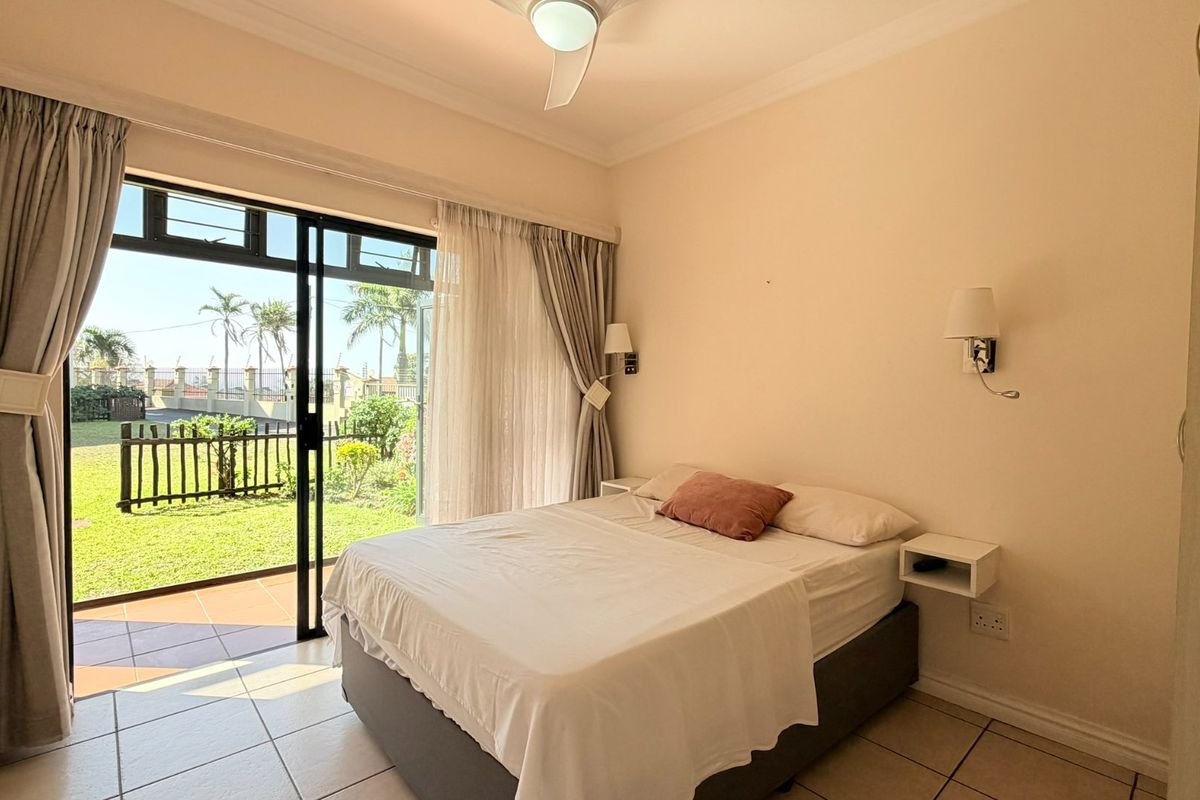 A bright bedroom featuring tiled flooring, wall-mounted lighting, and a large sliding glass door providing direct access to the outdoor garden area.