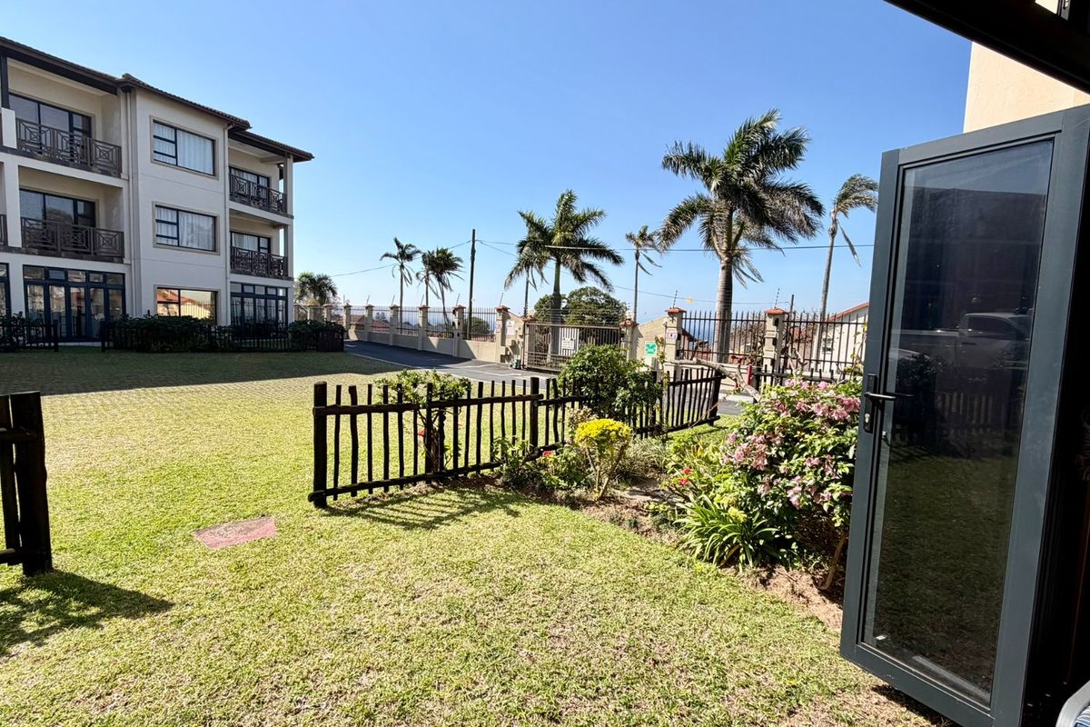 A well-maintained communal garden area featuring a manicured lawn, perimeter fencing, and established palm trees within an apartment complex setting.