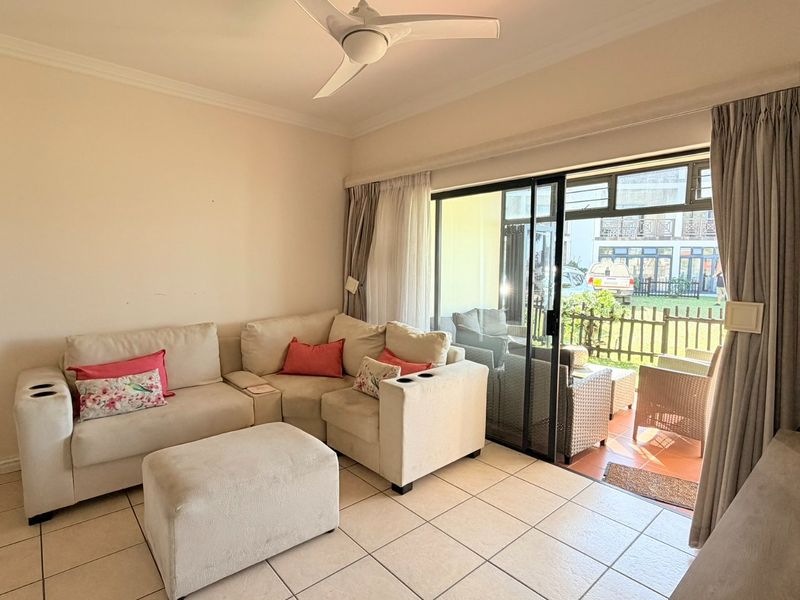 A bright living room featuring tiled flooring, a ceiling fan, and large sliding glass doors providing direct access to an outdoor patio area.