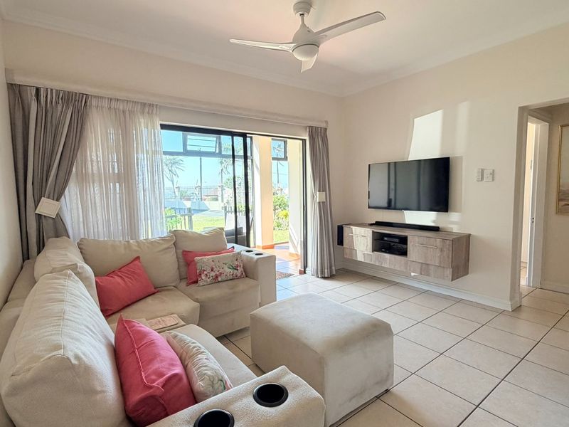 A bright living room featuring tiled flooring, a ceiling fan, and a sliding glass door providing access to the outdoor area.