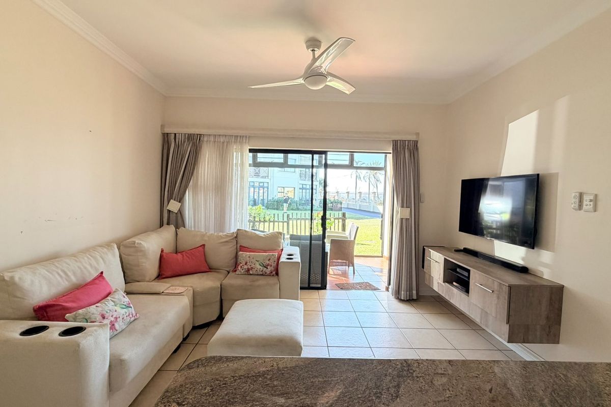 A bright living room featuring tiled flooring, a ceiling fan, and a sliding glass door providing direct access to an outdoor patio area.