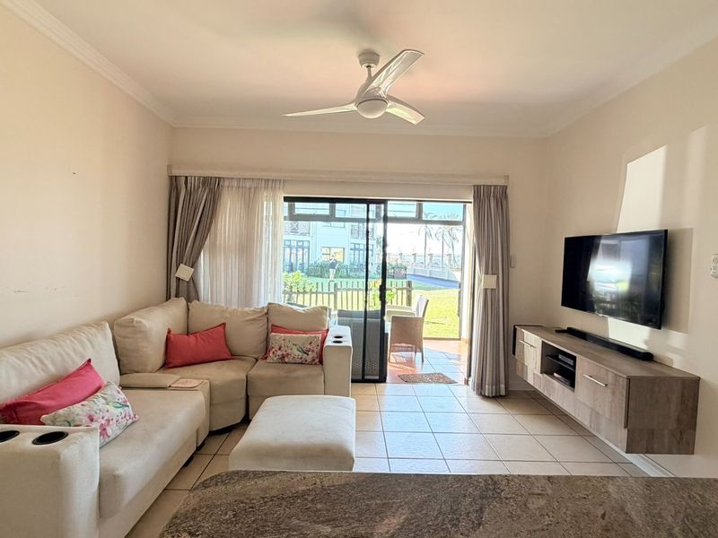 A bright living room featuring tiled flooring, a ceiling fan, and a sliding glass door providing direct access to an outdoor patio area.