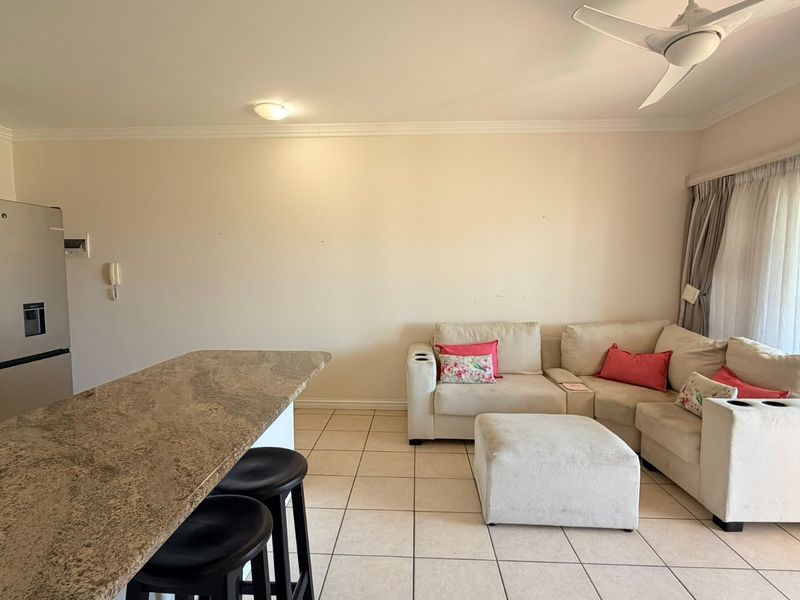 Open-plan living area featuring tiled flooring, a granite breakfast counter, ceiling fan, and direct access to an outdoor space via sliding glass doors.