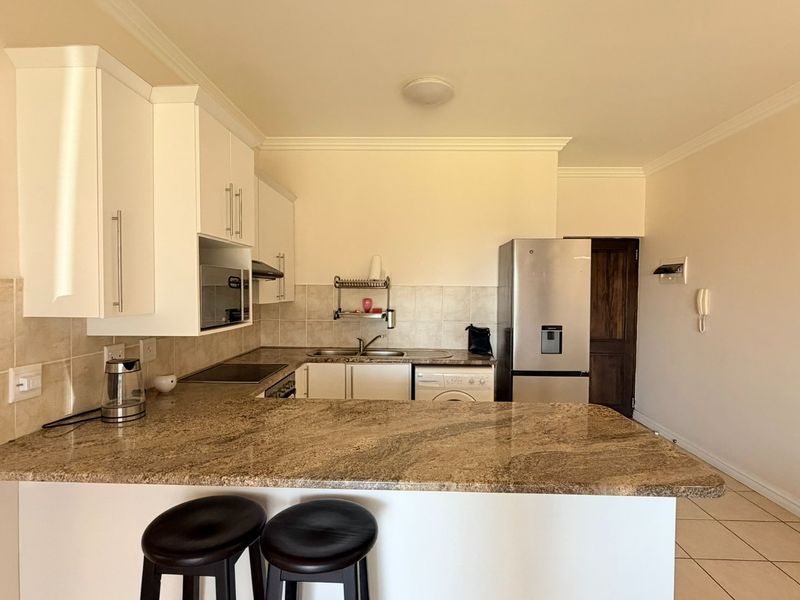 A functional kitchen featuring granite countertops, white cabinetry, tiled backsplash, and ceramic flooring, offering a practical layout for daily use.
