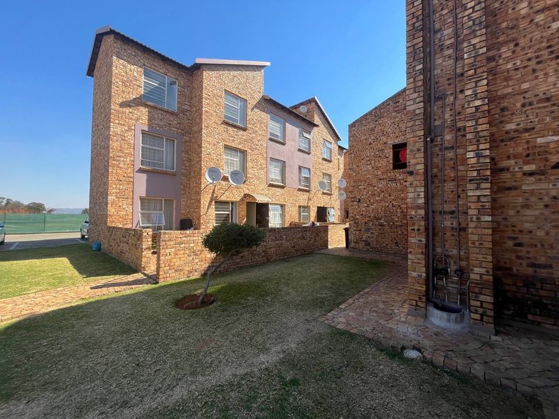 A view of the rear exterior of the apartment complex, featuring face brick construction, paved pathways, and a well-maintained lawn area.