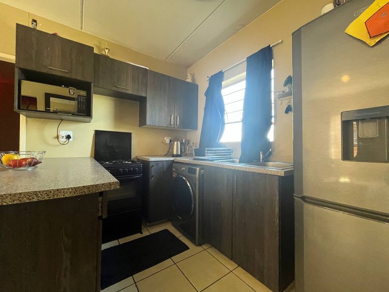 Compact kitchen featuring dark wood-look cabinetry, laminate countertops, tiled flooring, and integrated laundry plumbing, providing a functional workspace.