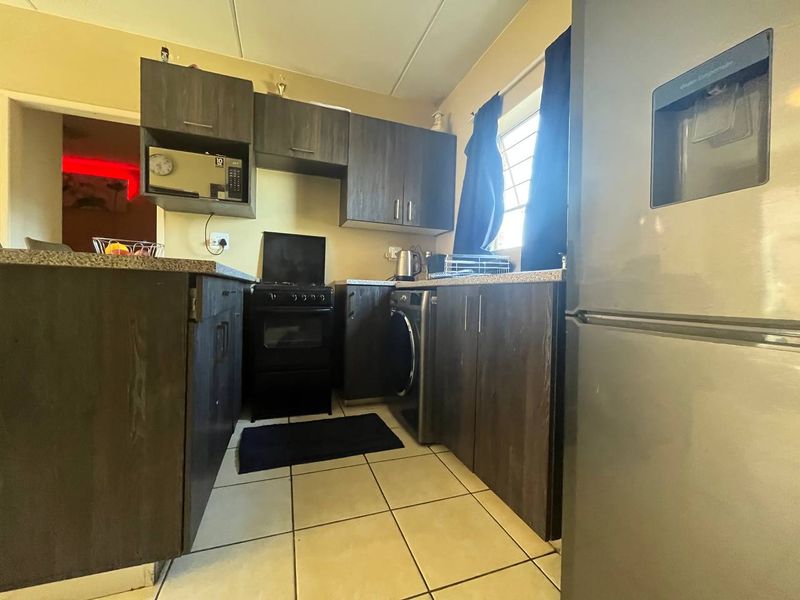 Compact kitchen featuring dark wood-look cabinetry, laminate countertops, tiled flooring, and space for a freestanding stove and laundry appliance.