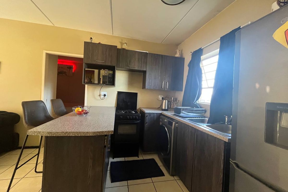 Compact kitchen featuring dark wood-finish cabinetry, laminate countertops, a breakfast bar, and tiled flooring, providing a functional workspace.