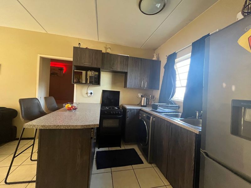 Compact kitchen featuring dark wood-finish cabinetry, laminate countertops, a breakfast bar, and tiled flooring, providing a functional workspace.