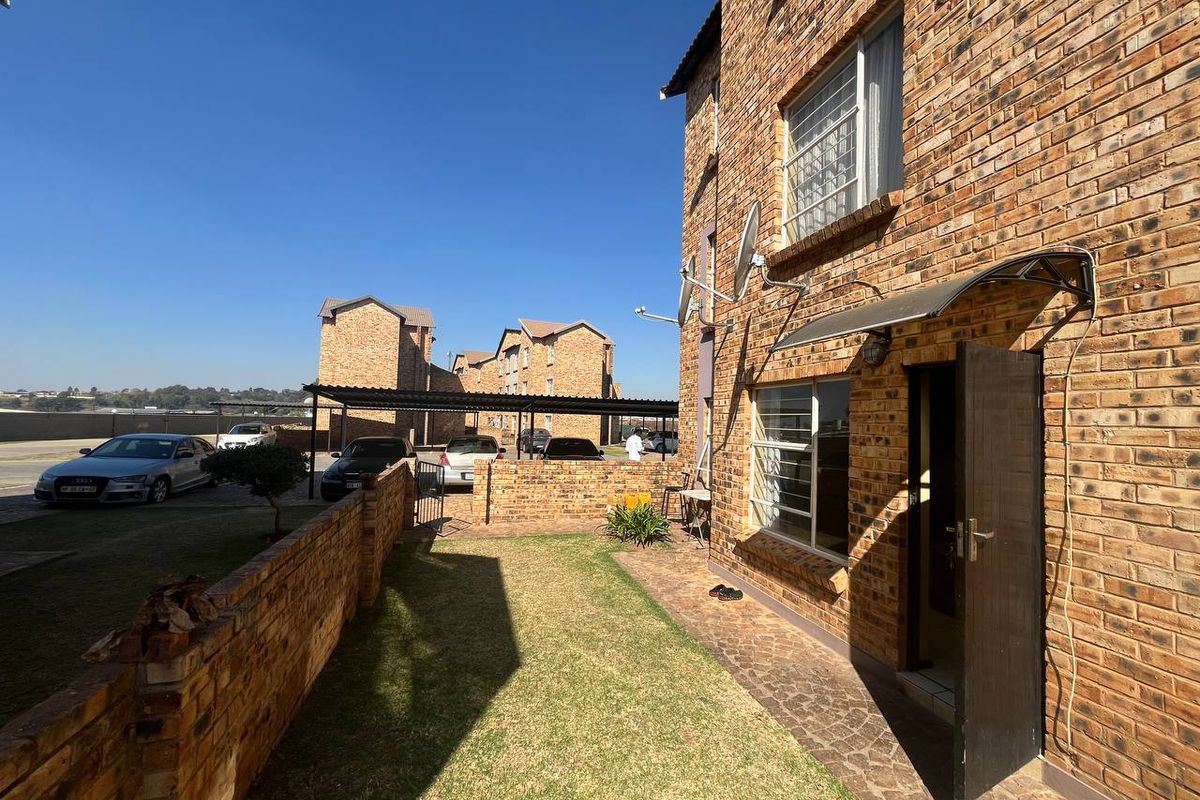 Rear exterior view of a face brick apartment building featuring a small private garden, paved walkway, and secure entrance.