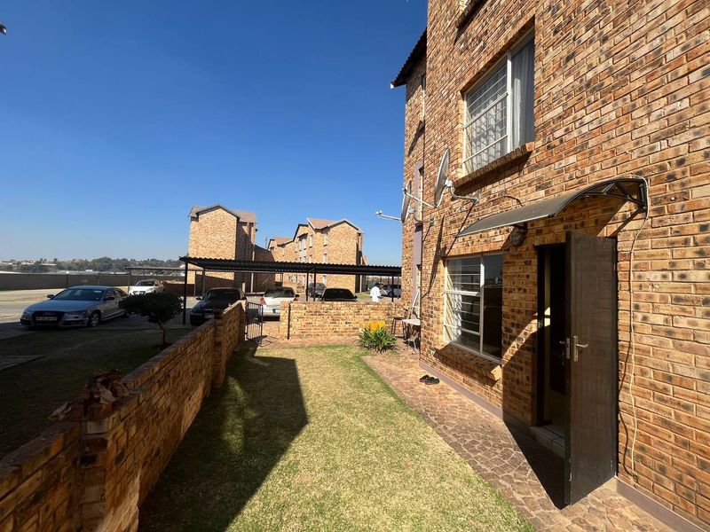 Rear exterior view of a face brick apartment building featuring a small private garden, paved walkway, and secure entrance.
