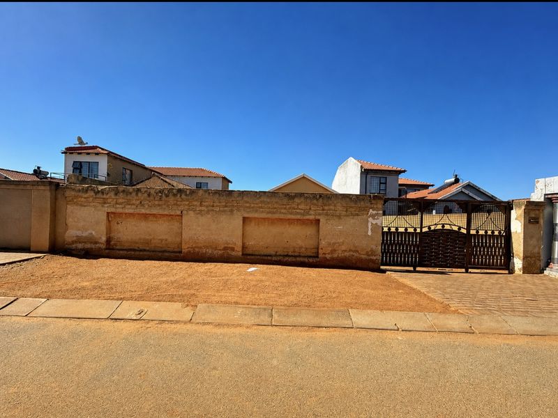 Front view of the property featuring a boundary wall, metal driveway gate, and paved entrance area.
